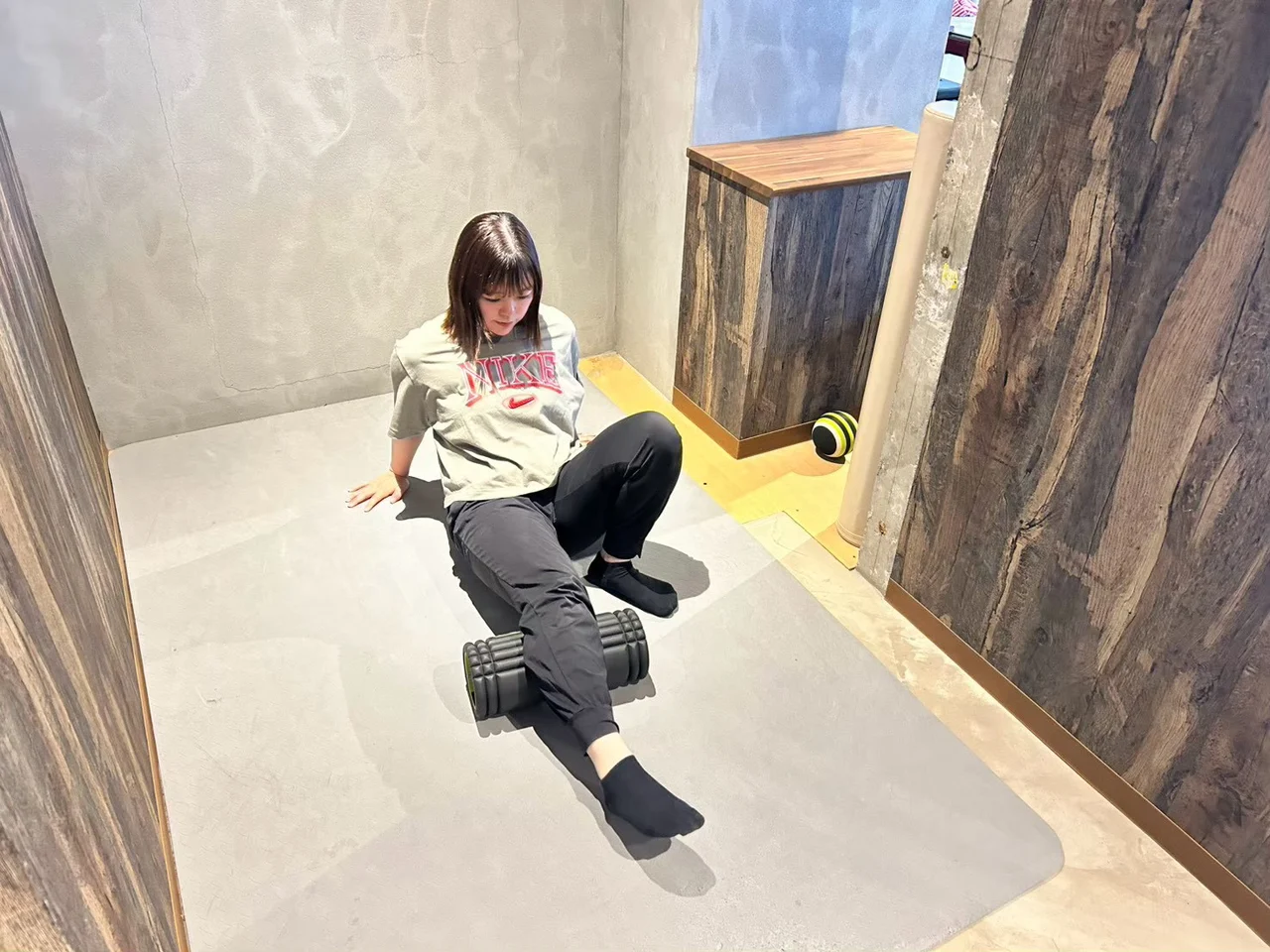梅ヶ丘店で、マットに座ってフォームローラーで脚をケアする女性